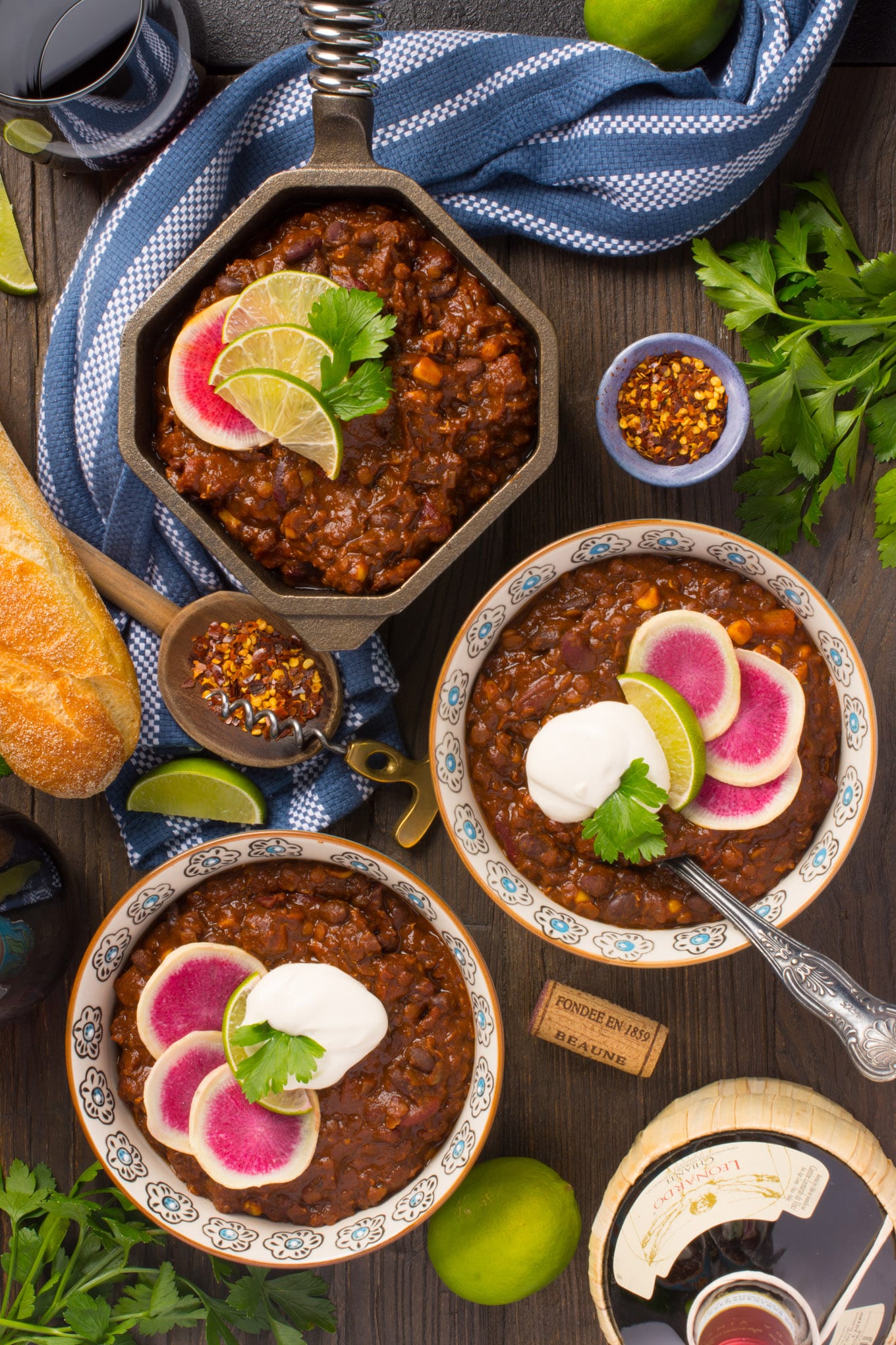 vegan mexican chili in bowls and small pot surrounded by bread, wine an spices