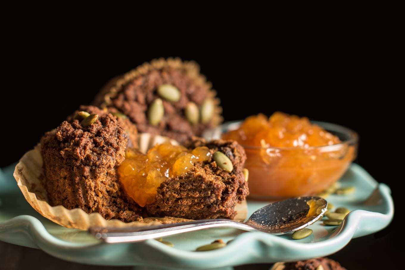 two pumpkin spice muffins with small bowl of apricot jam on cake stand