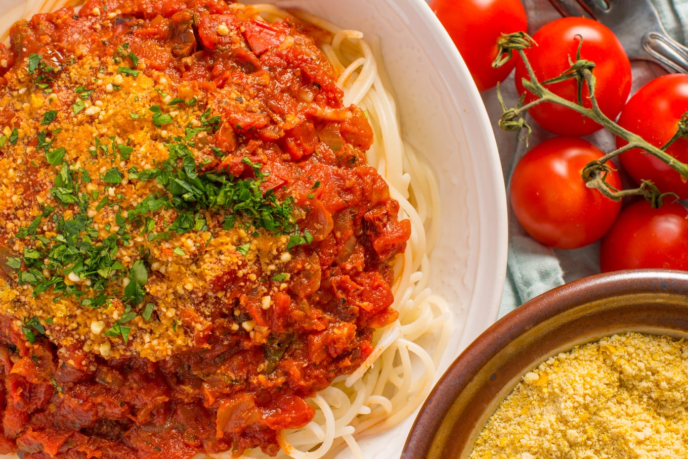 pasta with marinara sauce with vegan parmesan and fresh tomatoes to right