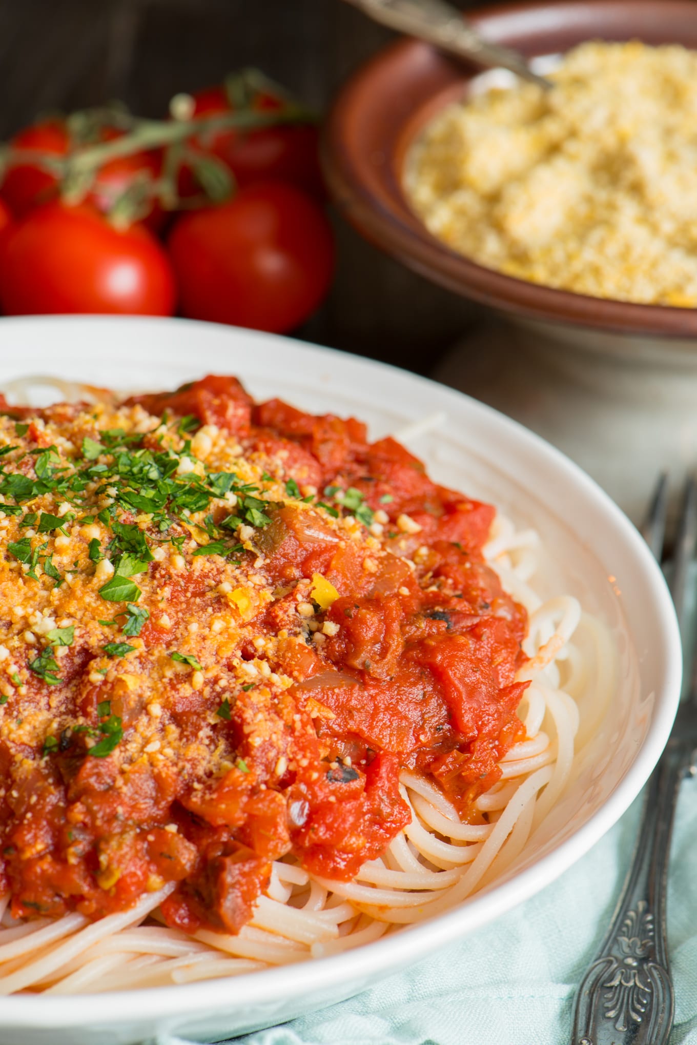 pasta with marinara sauce in bowl with vegan parmesan and tomatoes in background