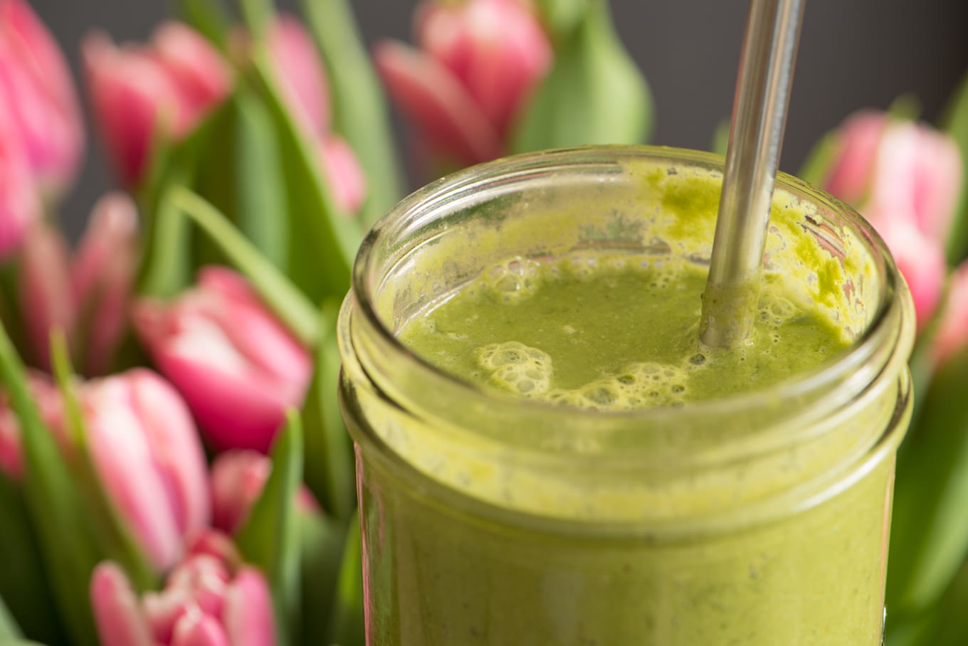 super greens smoothie in preserving jar with pink tulips in background
