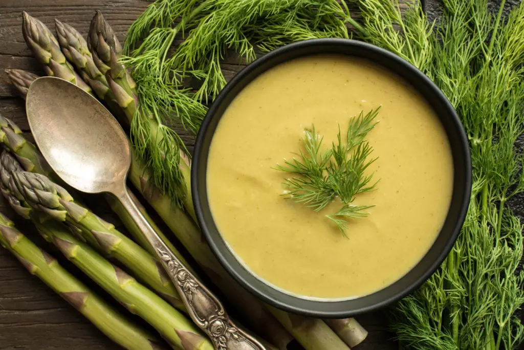 spring detox soup in bowl next to spoon, asparagus and dill weed