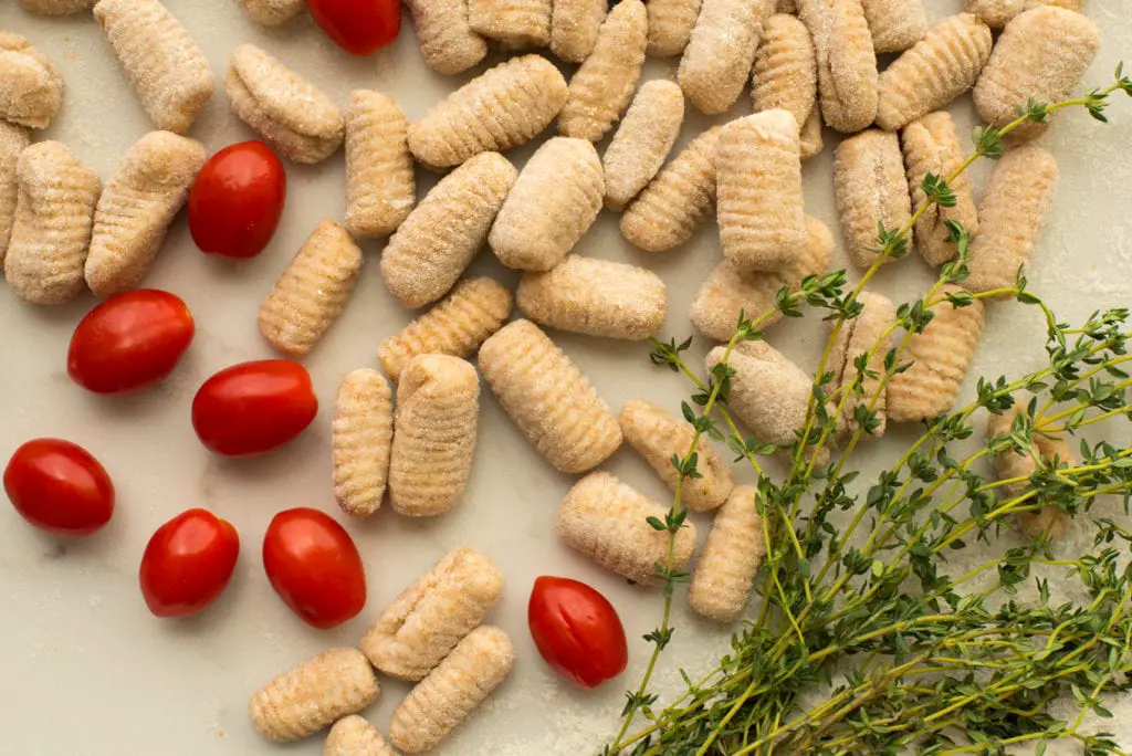 formed gnocchi next to sprigs of thyme and cherry tomatoes