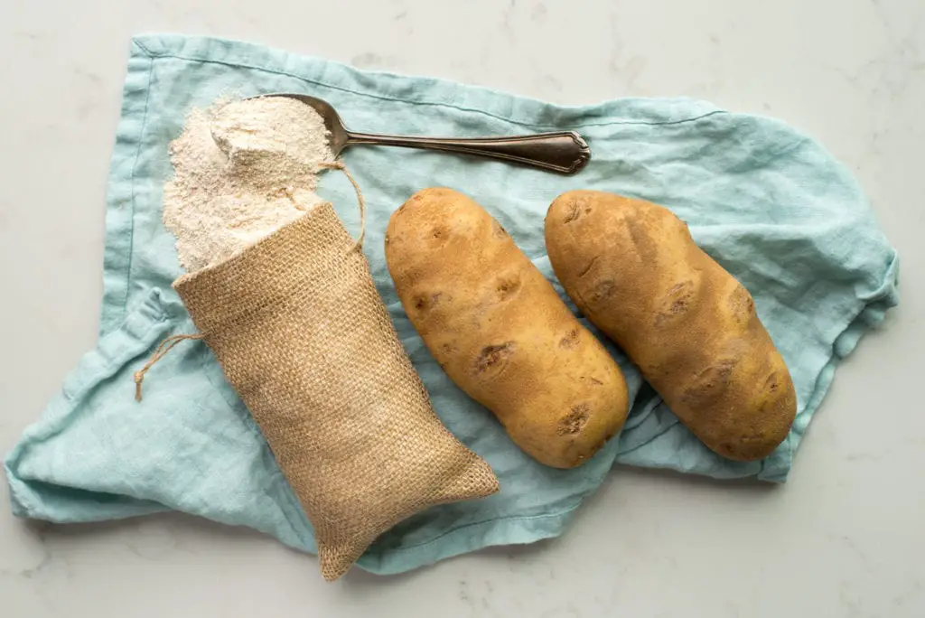 two russet potatoes and a mini bag of flour on a turquoise napkin