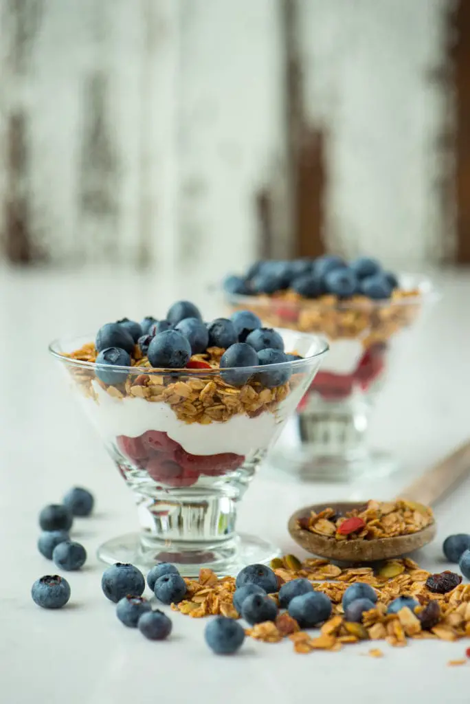 coconut yogurt parfait with berries and crunchy maple almond granola in two glasses
