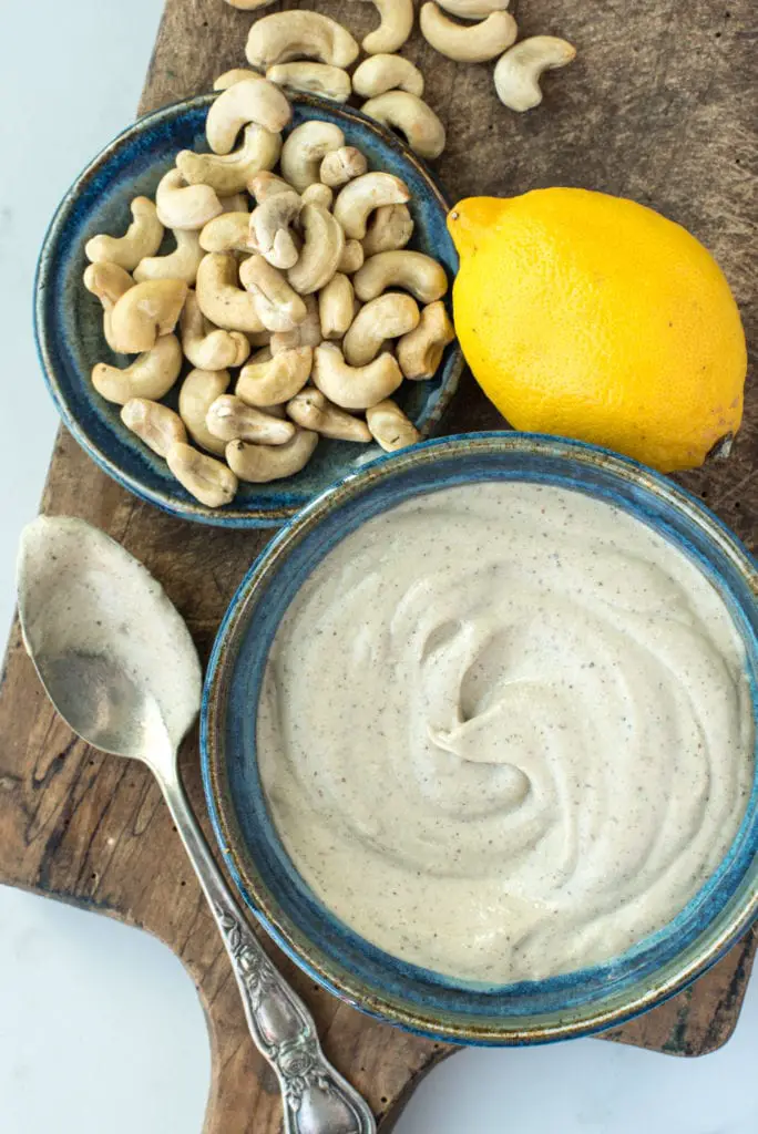 oil free caesar salad dressing in bowl next to cashews and lemon on cutting board