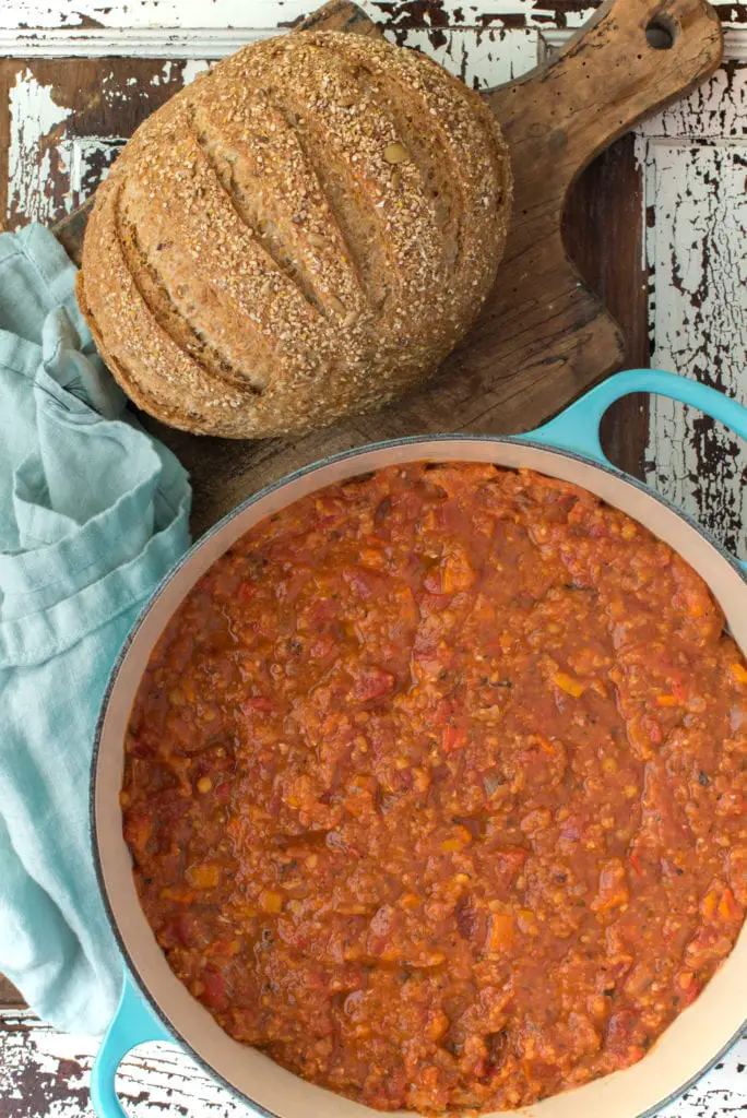 lentil bolognese in pot next to loaf of bread on cutting board