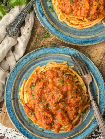 one pot lentil bolognese on spaghetti on two plates sitting on cutting board