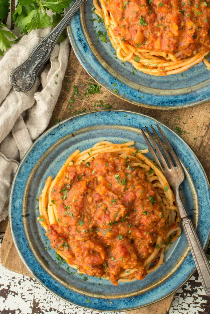 one pot lentil bolognese on spaghetti on two plates sitting on cutting board