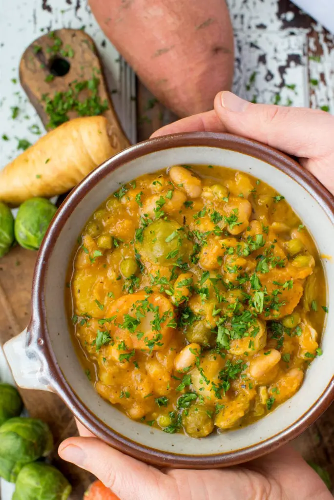 autumn vegetables and white bean stew in bowl being held