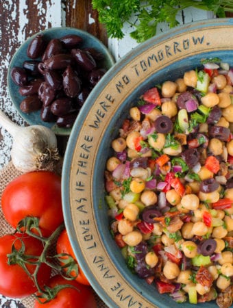 greek chickpea salad in bowl next to olives and tomatoes