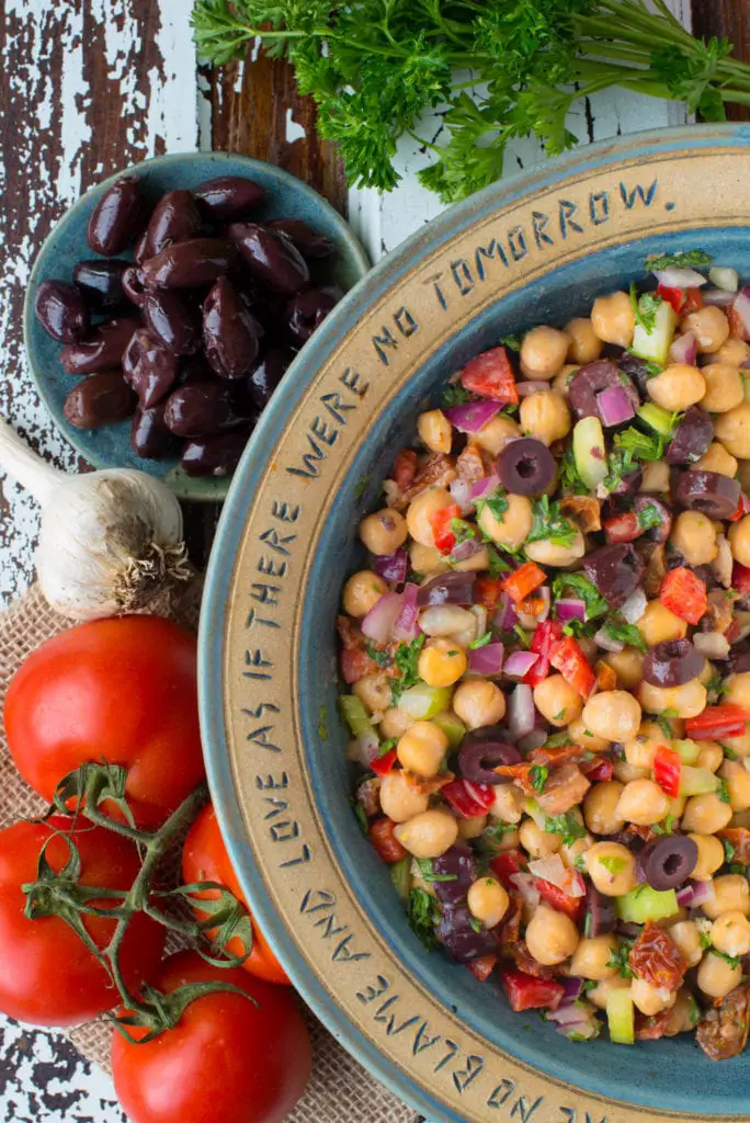 greek chickpea salad in bowl next to olives and tomatoes