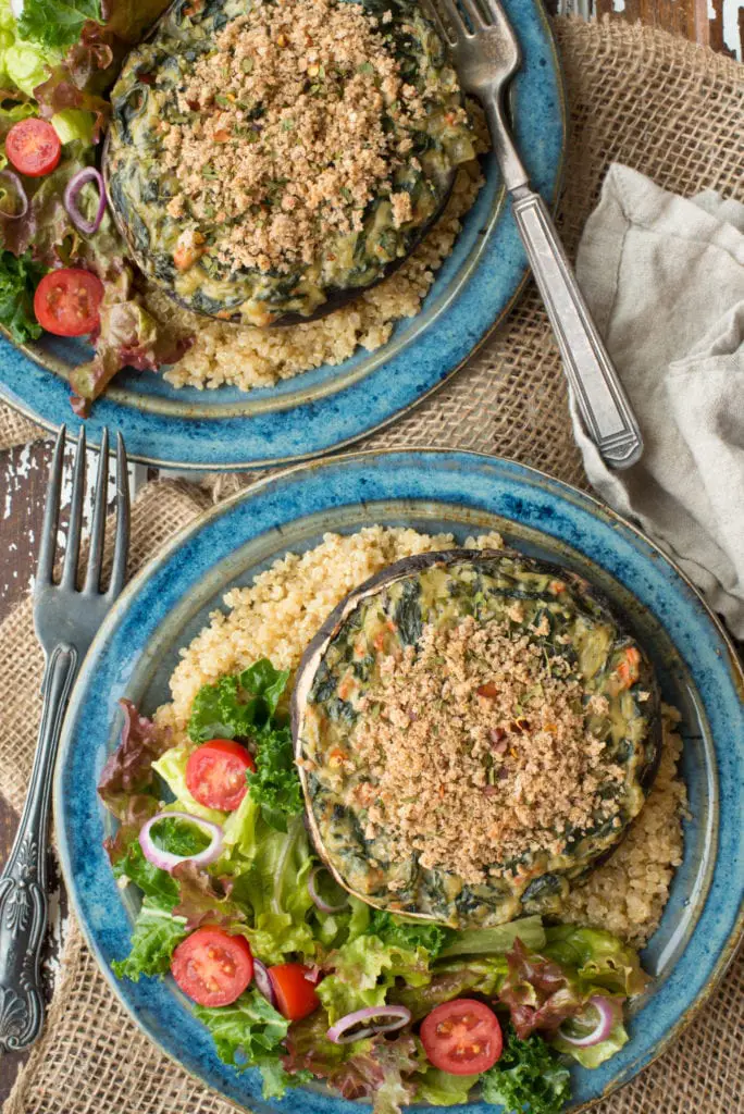 spinach stuffed portobello mushrooms on plates with quinoa and salad