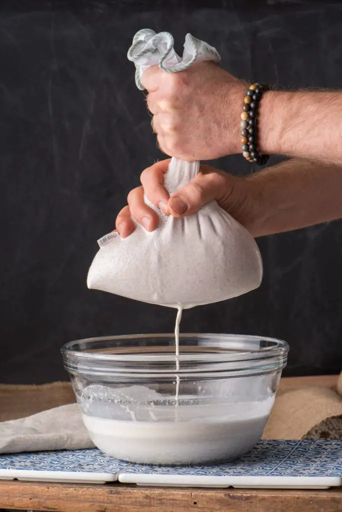 almond milk being squeezed through a nut milk bag