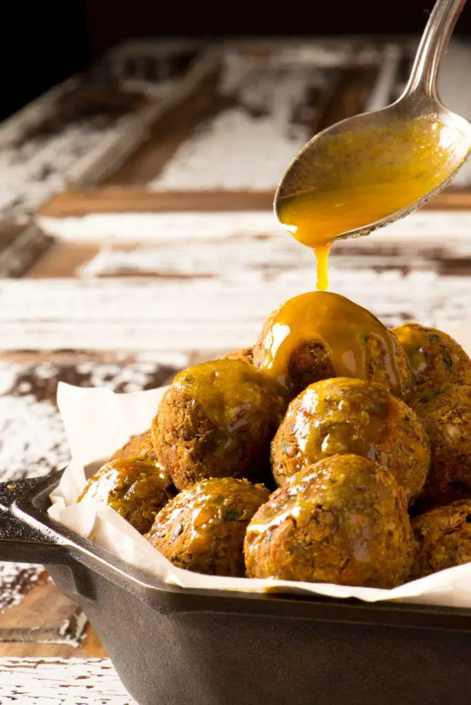 lentil balls in pan with sauce pouring over from spoon