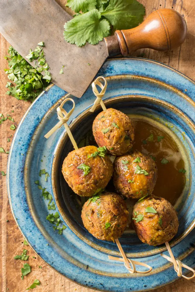 asian lentil balls on skewers in bowl next to herb chopping knife
