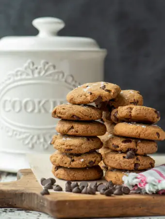 almond chocolate chip cookies stacked in front of cookie jar