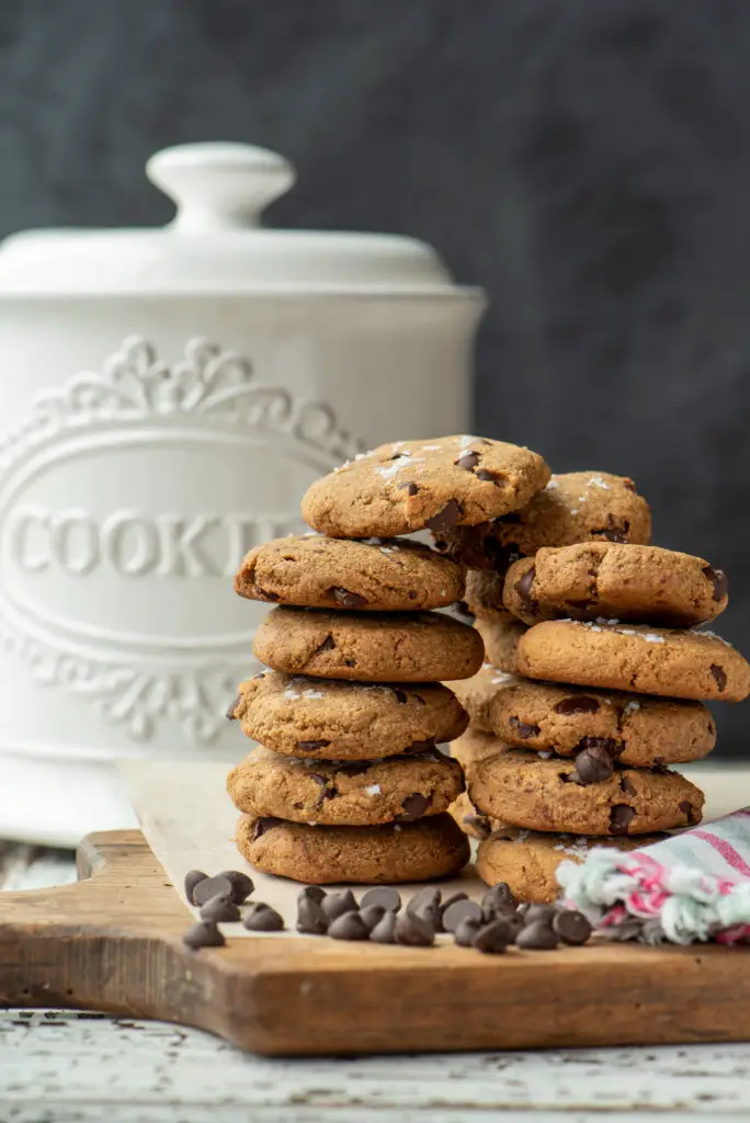 almond chocolate chip cookies stacked in front of cookie jar
