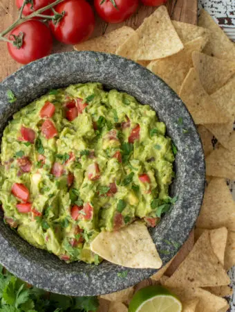 homemade guacamole in molcajete next to tortilla chips and tomatoes