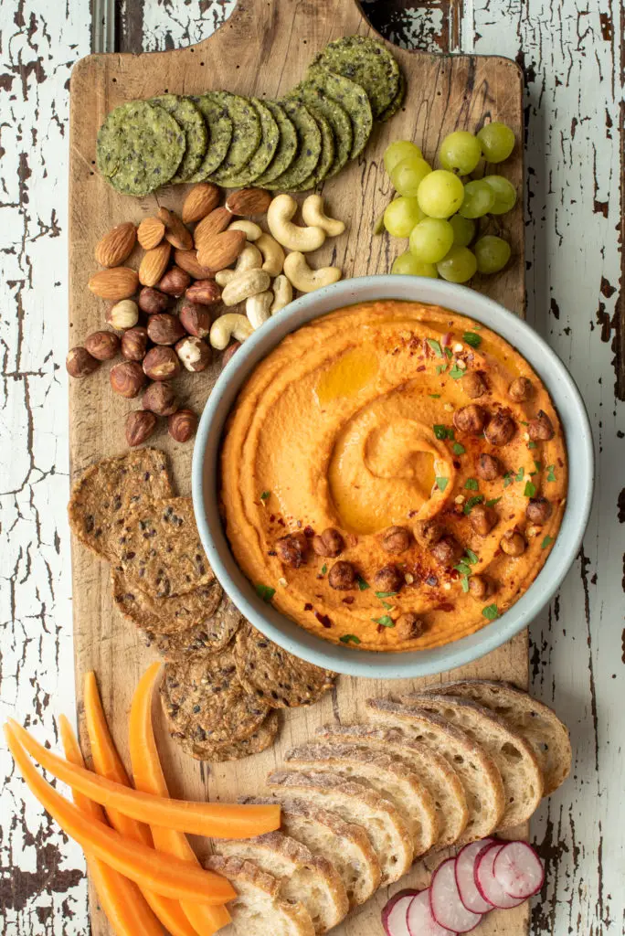 cutting board with crackers, nuts, grapes and hummus