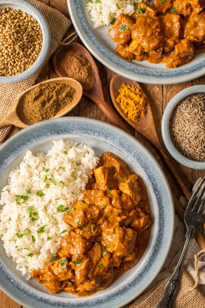 vegan butter tofu on two plates next to small bowls and wooden spoons filled with spices