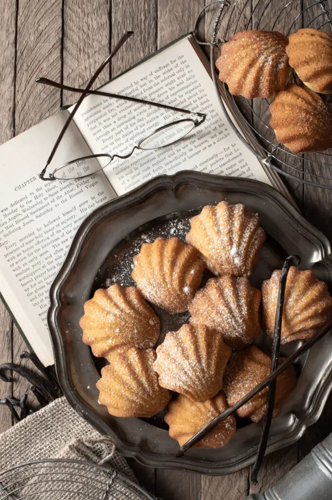 madeleines on pewter plate next to book and reading glasses