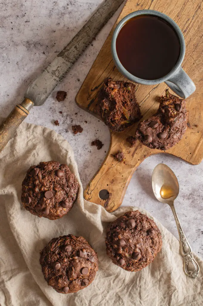 vegan double chocolate zucchini muffins on napkin and cutting board next to tea cup