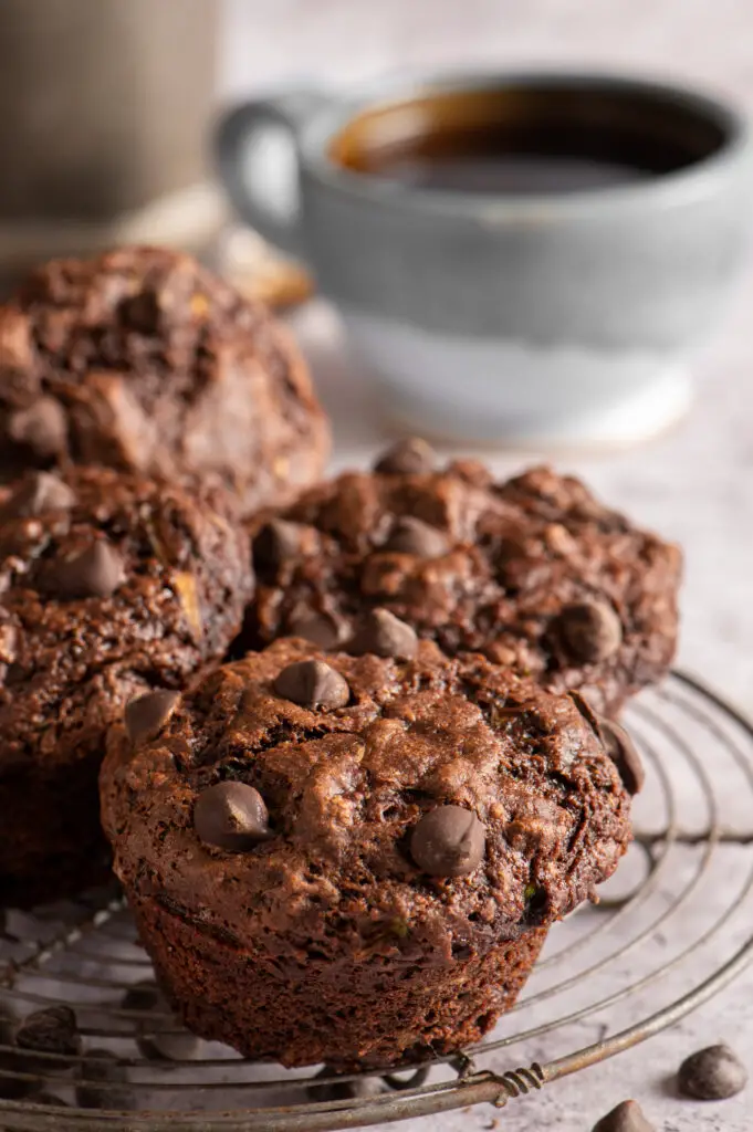 vegan double chocolate zucchini muffins on cooling rack next to tea cup