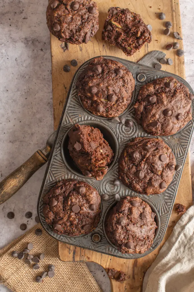 vegan double chocolate zucchini muffins in muffin tin sitting on cutting board