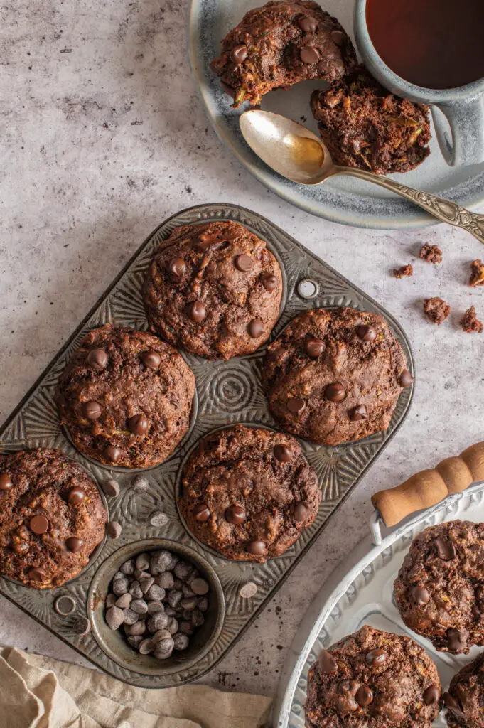 vegan double chocolate zucchini muffins in muffin tin and tray next to tea cup