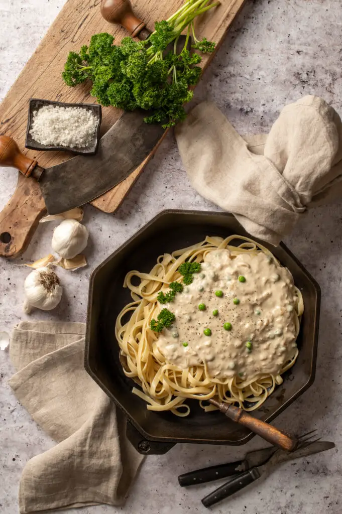 vegan pasta alfredo in skillet next to parsley on cutting board