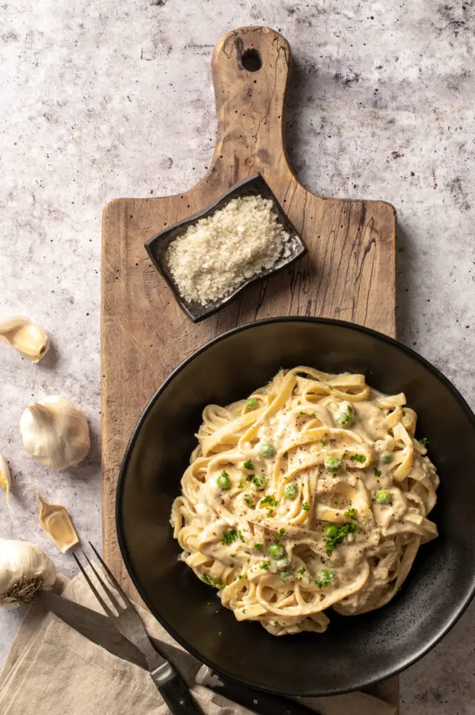 vegan pasta alfredo in black bowl on cutting board next to small dish with course sea salt