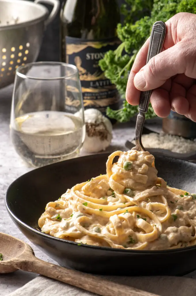 vegan pasta alfredo in black bowl with hand swirling pasta in bowl