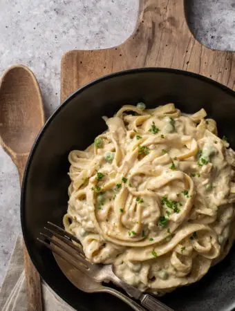 vegan pasta alfredo in black bowl on cutting board