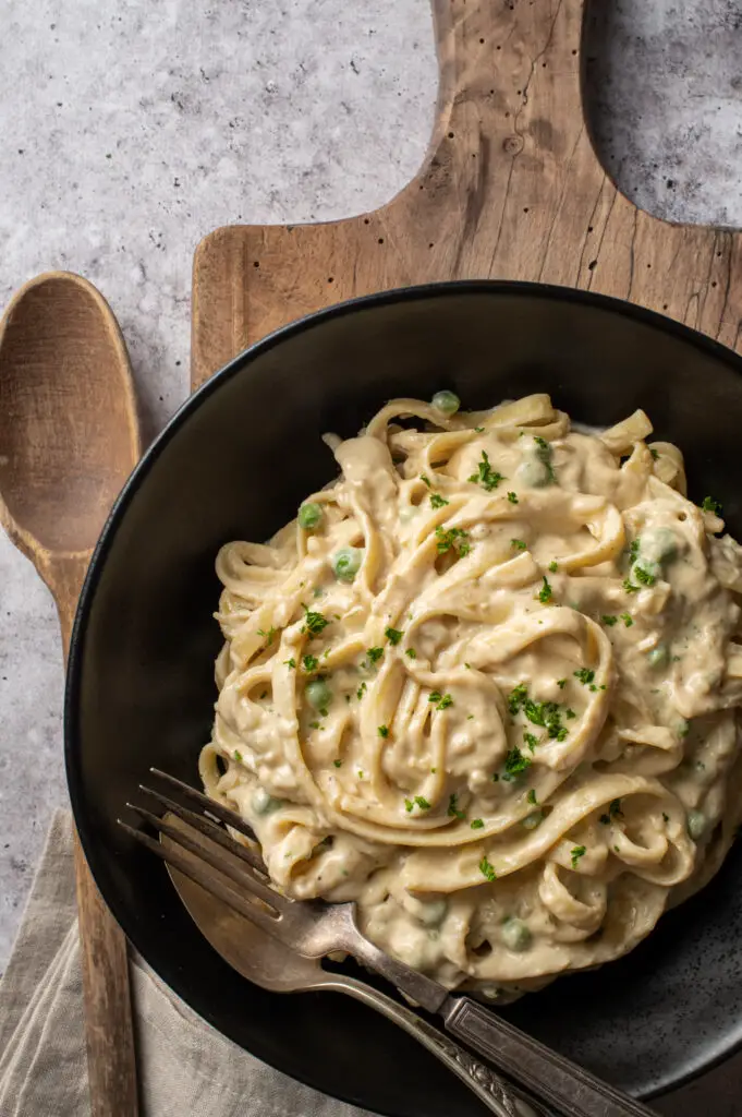 vegan pasta alfredo in black bowl on cutting board