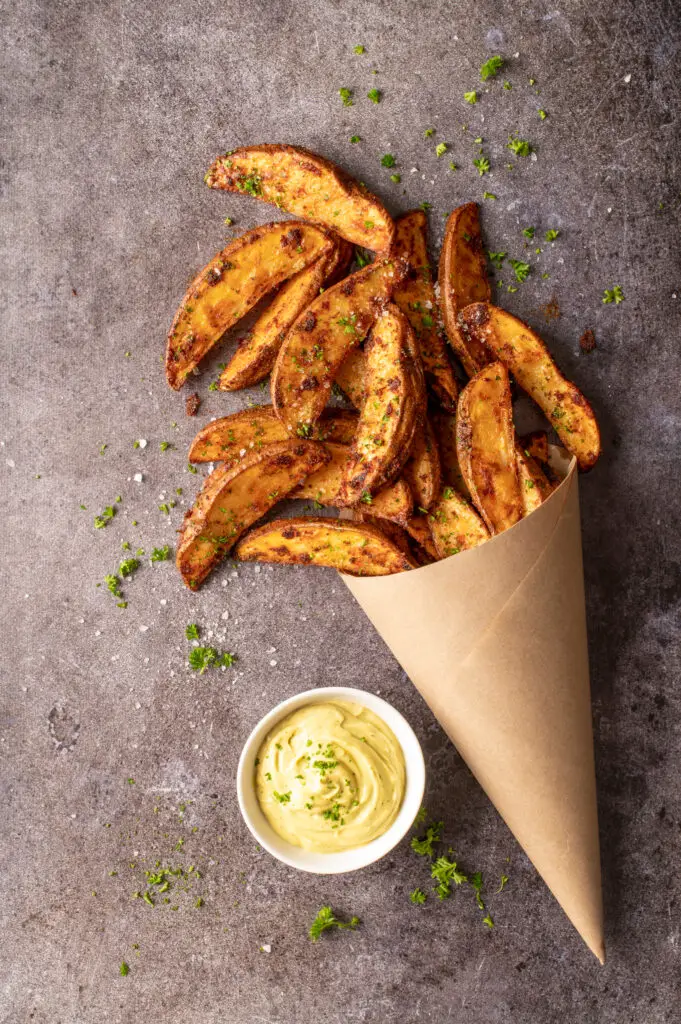 crispy oven potato wedges in paper cone next to dish of avocado mayo