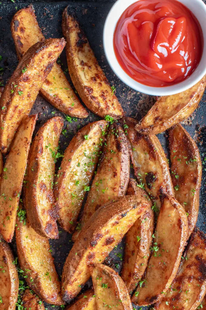 crispy oven potato wedges on baking sheet with small dish of ketchup