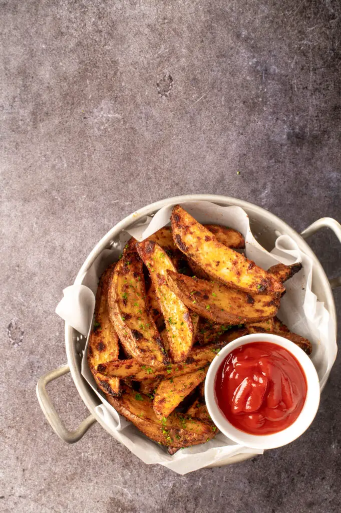 crispy oven potato wedges in colander with small dish of ketchup