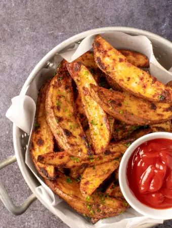 crispy oven potato wedges in colander with small dish of ketchup