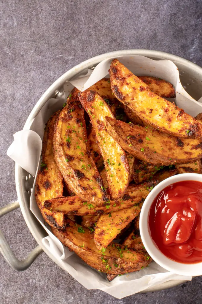 crispy oven potato wedges in colander with small dish of ketchup
