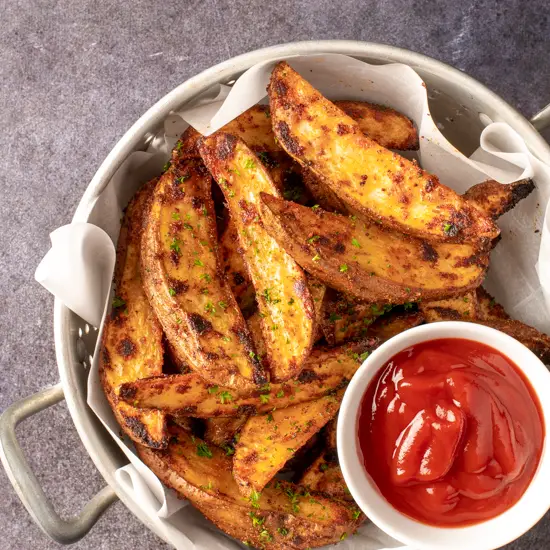 crispy oven potato wedges in colander with small dish of ketchup - recipe image