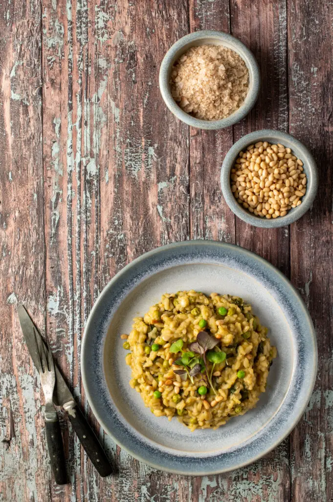 spring pesto risotto on blue pottery plate next to bowls of pine nuts and sea salt