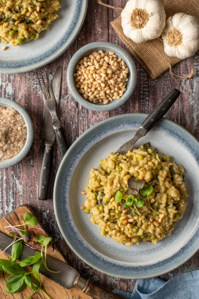 spring pesto risotto on two blue pottery plates next to bowl of pine nuts