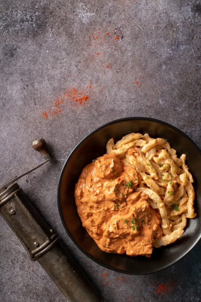 vegan hungarian tofu paprikash in black bowl next to vintage spice grinder