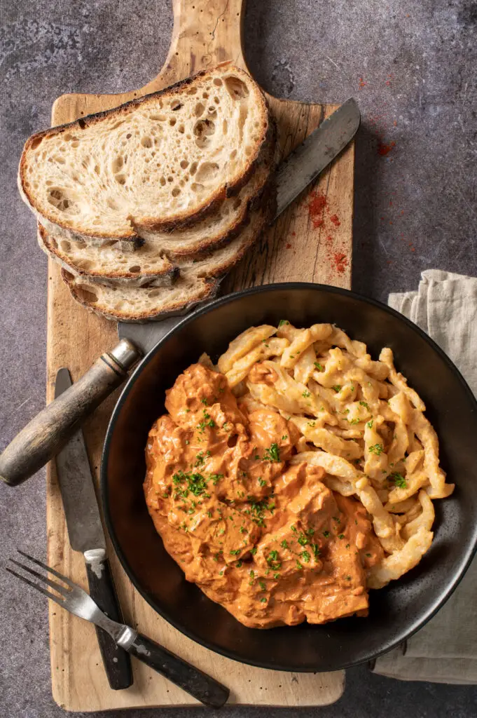 vegan hungarian tofu paprikash in black bowl on cutting board next to three slices of sourdough