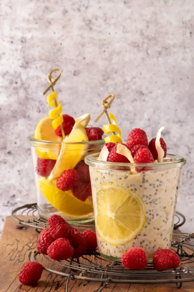 creamy lemon overnight oats in glass jars with lemons and raspberries in another glass jar