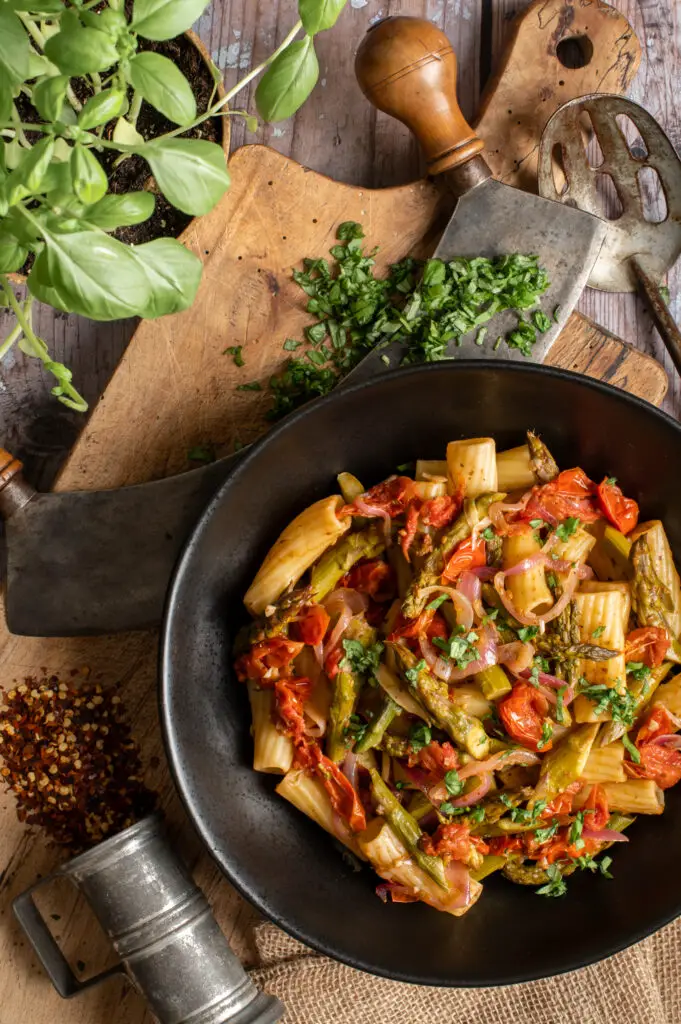 simple asparagus rigatoni in black bowl on cutting board with herb chopper