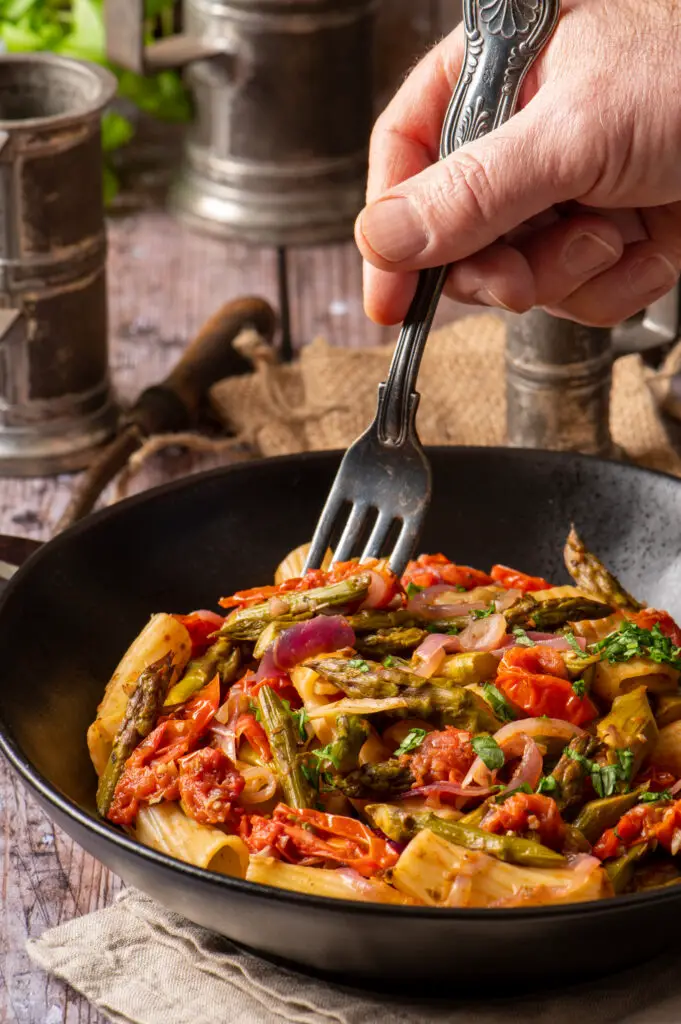 simple asparagus rigatoni in black bowl with hand holding fork in bowl