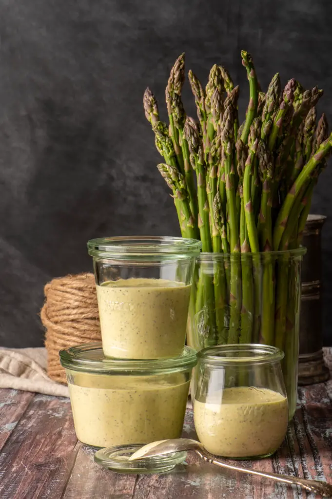 vegan lemon poppyseed dressing in three glass jars next to jar of asparagus