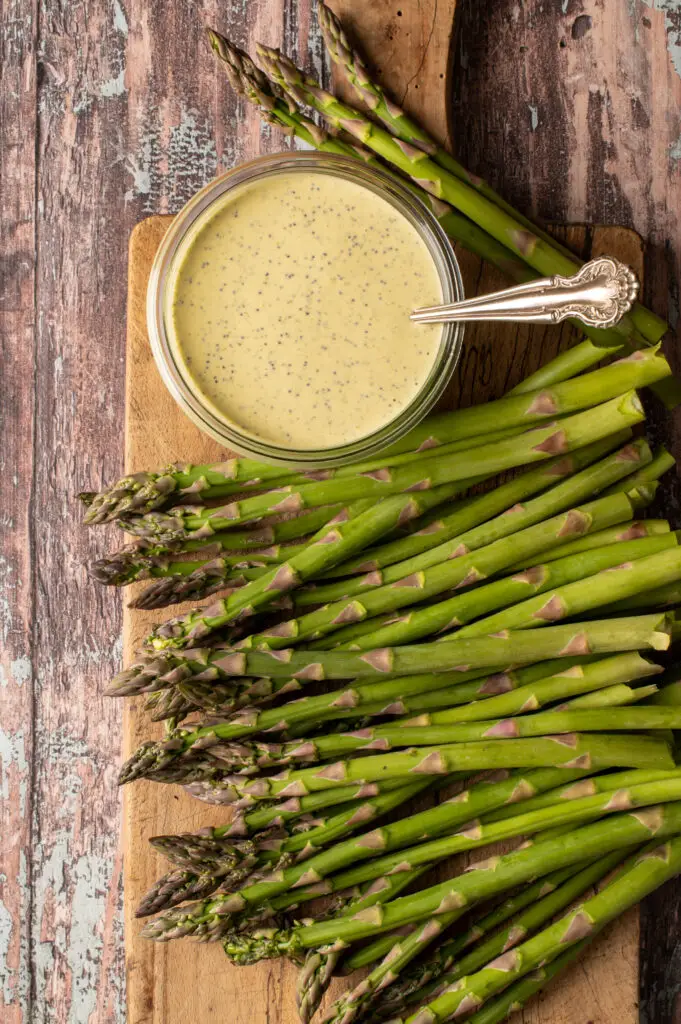 vegan lemon poppyseed dressing in glass jar on cutting board next to asparagus